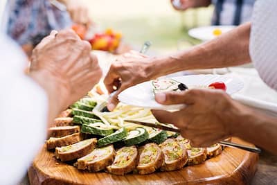 Close-up of unrecognizable people putting food on their plates. Family celebration outside in the backyard. Big garden party.