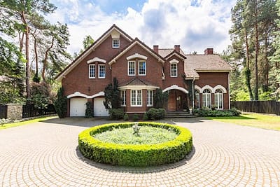 Front view of a driveway with a round garden and big, english style house in the background. Real photo